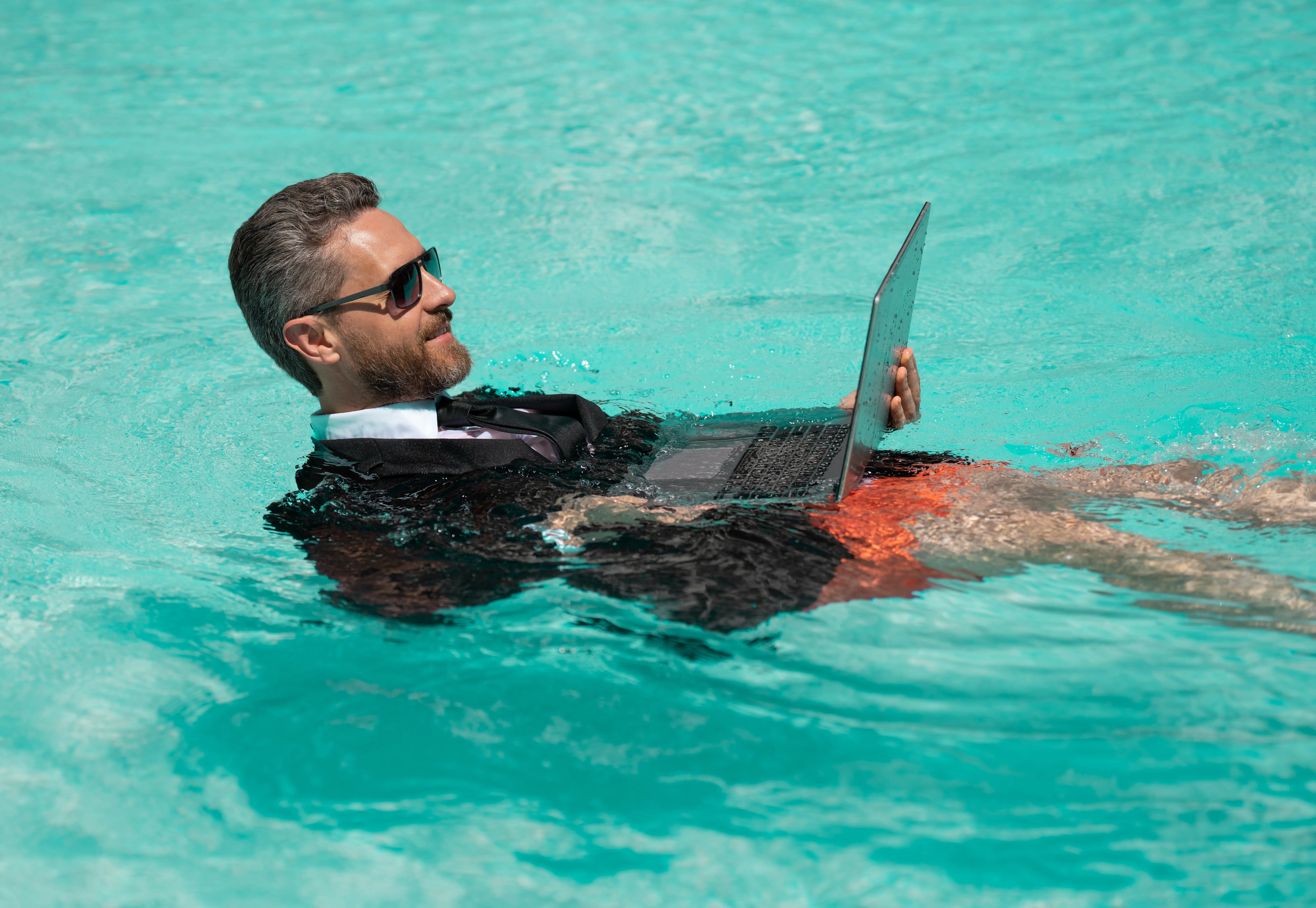 Ein Mann hat am Wochenende ein geschäftliches Videotelefonat und erfrischt sich dabei am Pool.