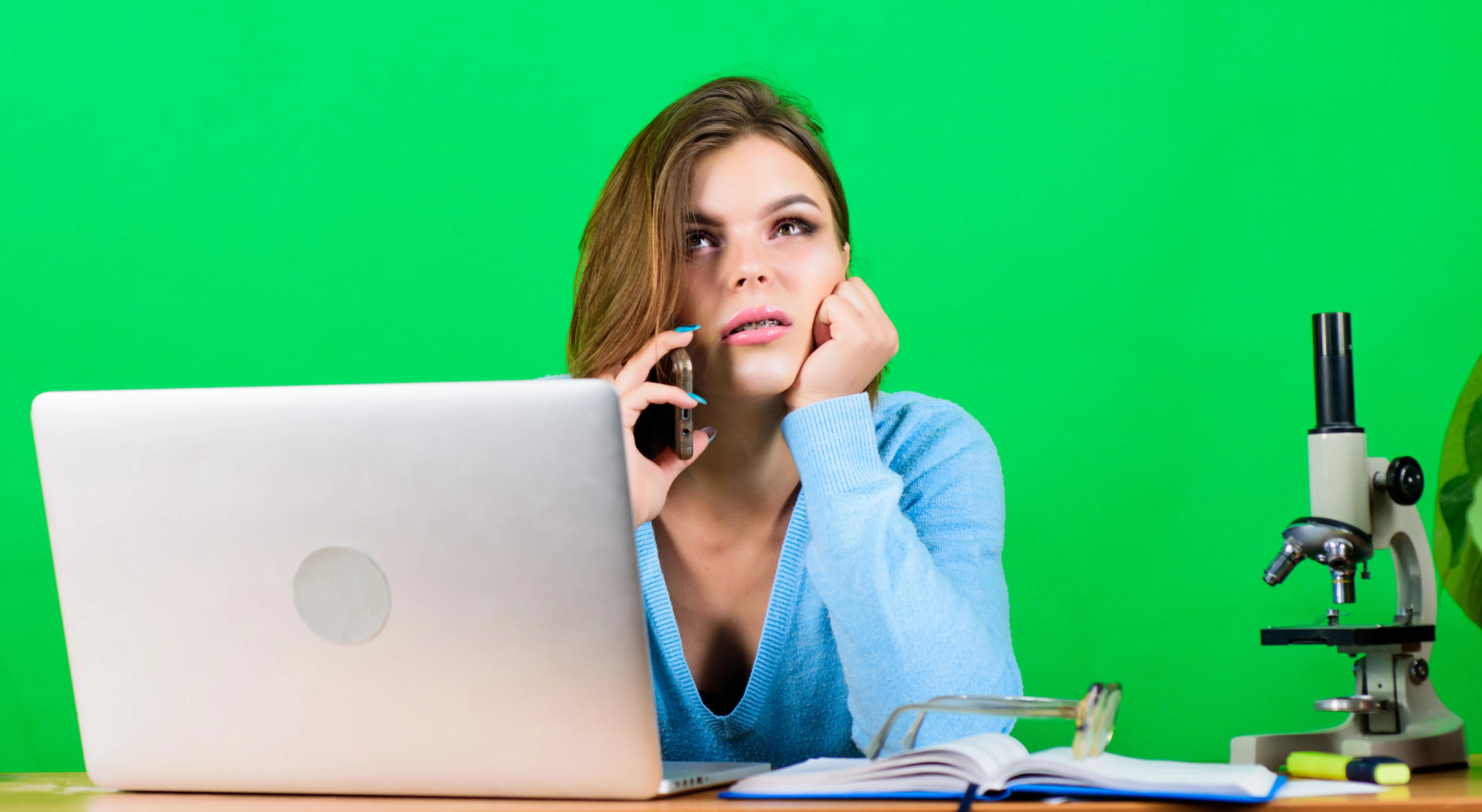 Moderne, attraktive Studentin mit Laptop: Bildungskonzept und Studentenleben – sie telefoniert mit einer Freundin, nimmt an Online-Fernkursen teil, kauft online ein, erledigt Hausaufgaben und plaudert statt zu lernen.